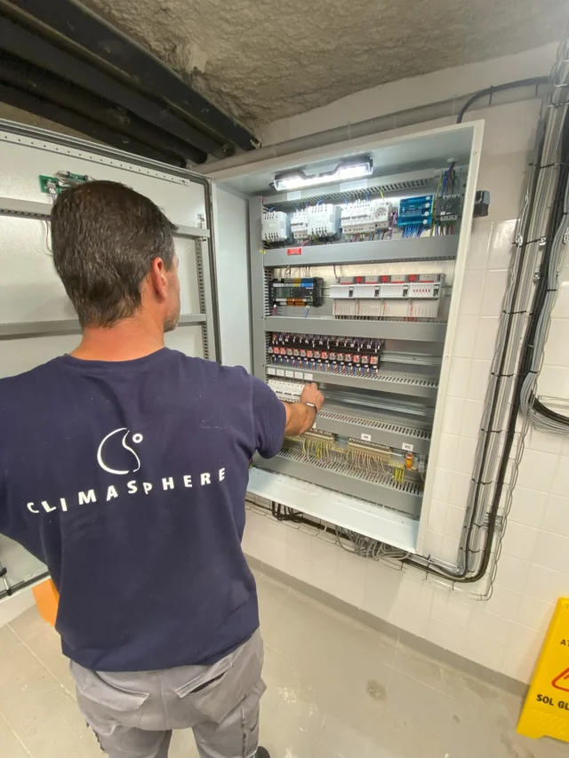 Technicien inspectant le tableau de commande du système hybride solaire de l'OCDE.